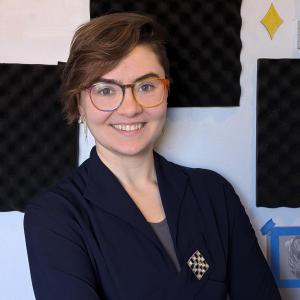 Front-facing person with short hair and glasses, smiling at the camera.